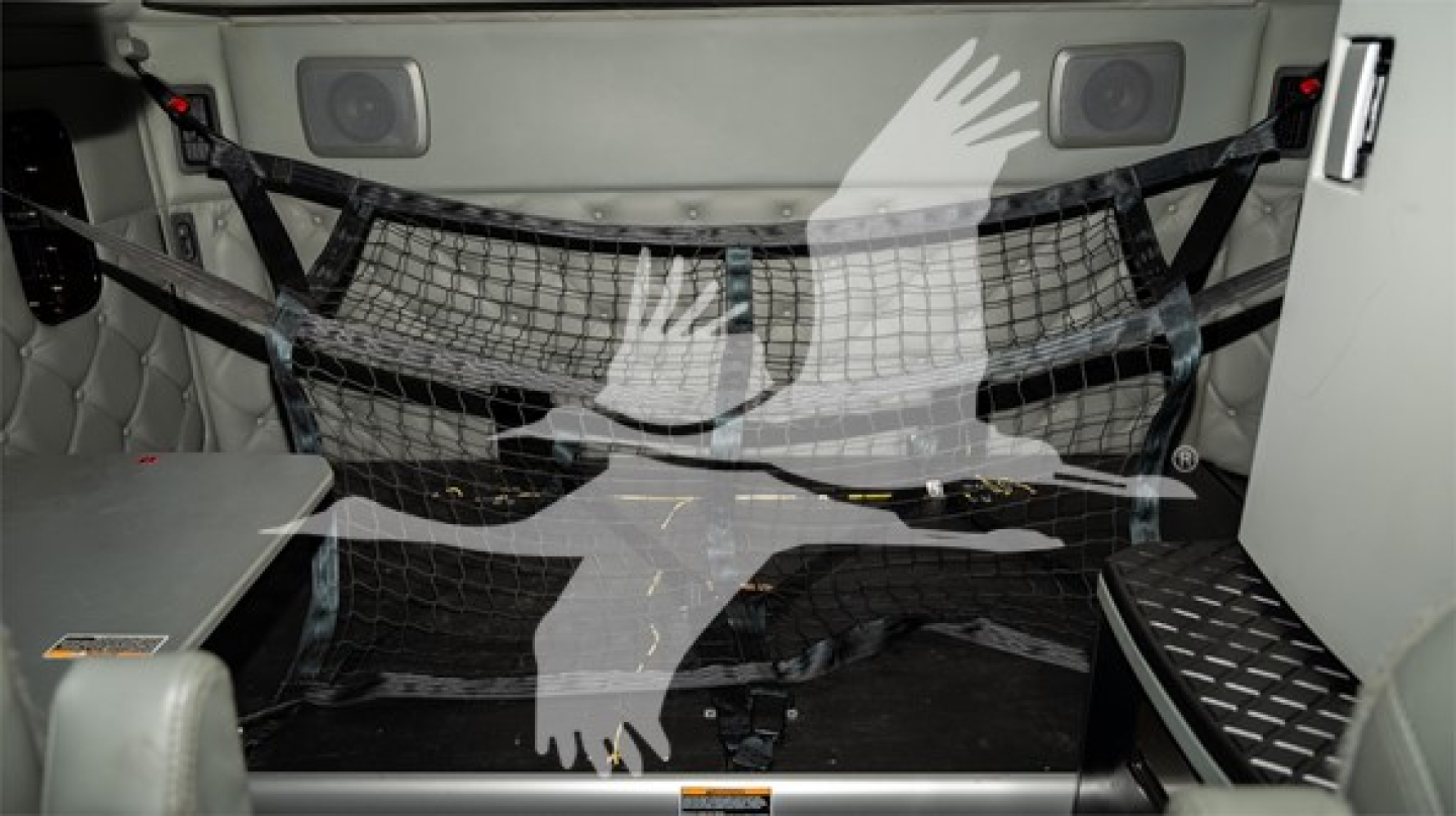 Interior of a Kenworth truck cab showing a safety net/strap net across the rear cargo area and storage panels.