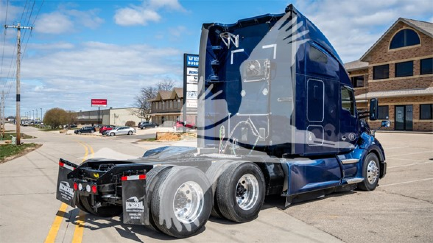 Kenworth T680 conventional sleeper tractor with blue and black graphics, rear view show cab and dual rear axles, trailer hitch, street scene