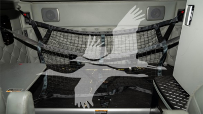 Interior of a Kenworth truck cab showing a safety net/strap net across the rear cargo area and storage panels.