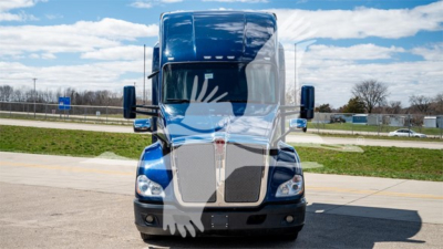 Kenworth T680 front view showing large grille and blue cab with sleeper, truck in a lot.
