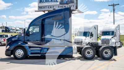 Kenworth T680 tractor shows blue cab with sleeper, front windshield, and dual rear axles. Visible sign in background reads Kordell and Next Exit. No detailed labels visible on the vehicle.