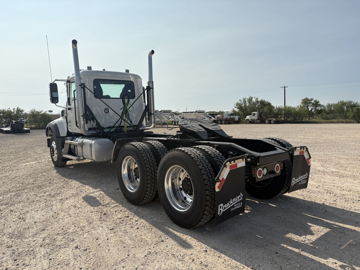 Mack GR64FT conventional daycab chassis showing dual rear axles, fifth wheel hitch, fuel tanks, and dual exhaust stacks visible from rear-left angle.