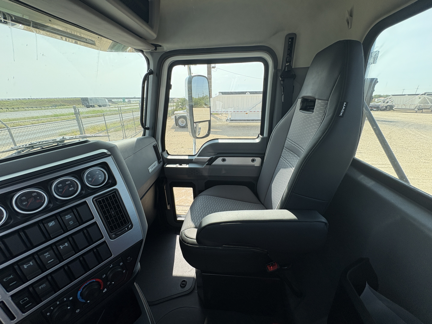 Cab interior of a 2027 Mack GR64FT truck showing dashboard gauges, steering wheel, driver seat, and large side window.