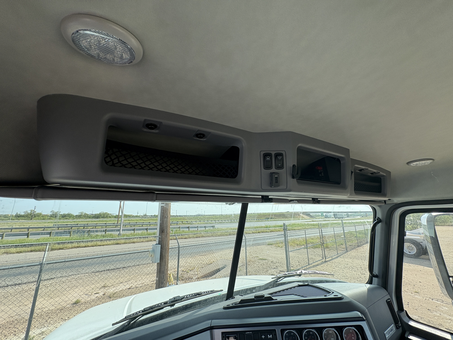 Truck cab interior overhead console area with vent, control switches, and sun visor in a Mack GR64FT. Dashboard and windshield visible.