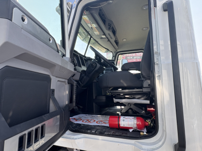 Cab interior of a 2027 Mack GR64FT truck with open door shows driver seat, dashboard, and a red fire extinguisher on the floor; VIN and stock number not visible in this view.
