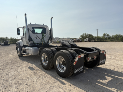 Mack GR64FT conventional daycab chassis showing dual rear axles, fifth wheel hitch, fuel tanks, and dual exhaust stacks visible from rear-left angle.