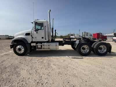 Truck side view showing a white Mack GR64FT conventional daycab chassis with dual rear axles and aluminum fuel tank; no visible cab interior text.