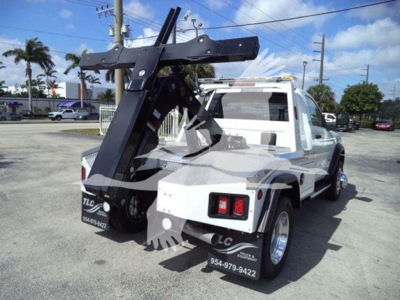 Truck bed with a mounted heavy-duty winch crane on a white Ram 5500 SLT towing vehicle, side view showing front cab and rear hitch area.