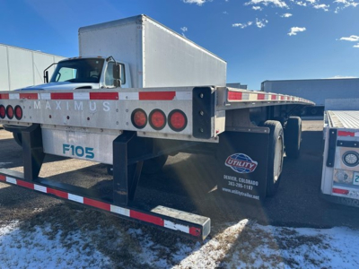 Flatbed trailer rear view showing Maximus branding and F105 on the mudguard, utility logo, and reflective red/white striped underride guards.