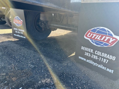 Utility logo mudflaps on a trailer showing 'DENVER, COLORADO' and contact info; wheel and undercarriage visible.