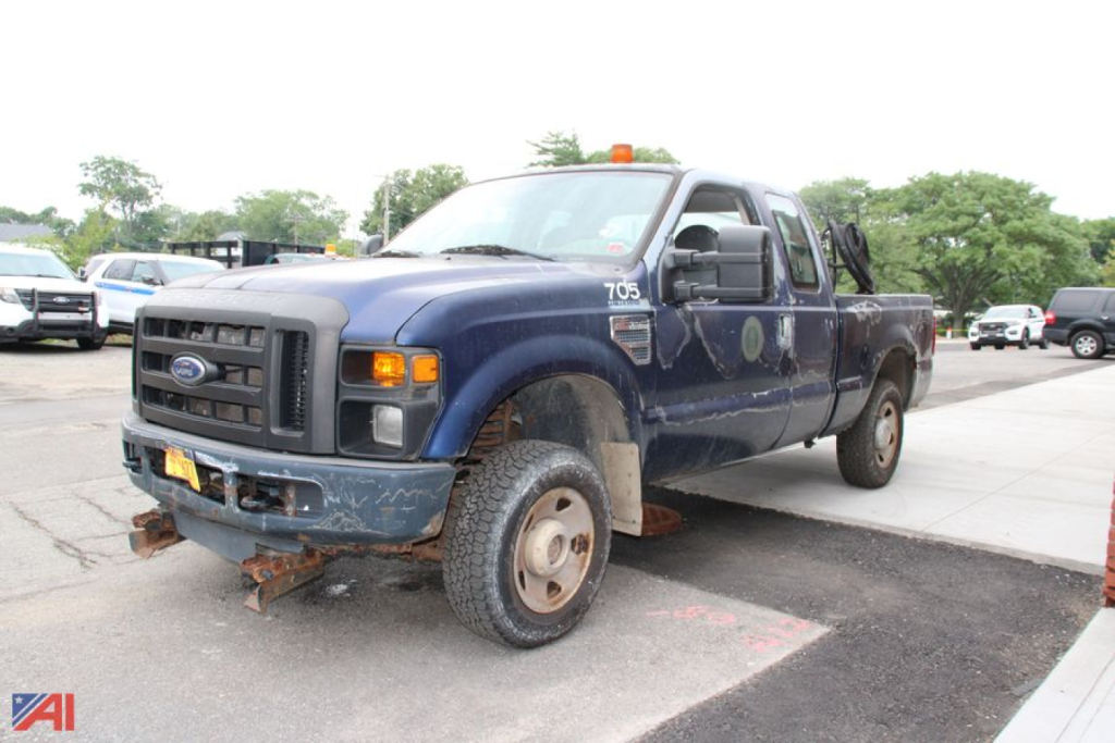 Ford F-250 Super Duty pickup truck with extended cab, blue exterior, showing front grille and bumper, large tires, and rusted front hitch area.
