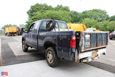 Ford F-250 Super Duty pickup viewed from rear-left, with a utility bed, ladder rack, and equipment in a lot.