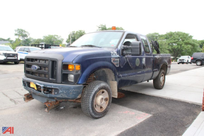 Ford F-250 Super Duty pickup truck with extended cab, blue exterior, showing front grille and bumper, large tires, and rusted front hitch area.