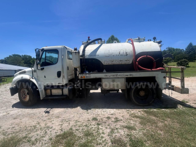 Freightliner M2 106 vacuum truck side view showing cylindrical tank with hoses and controls. Vehicle details include VIN plate and stock number area visible on side.