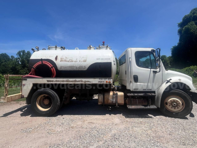 Freightliner M2 106 vacuum truck side view showing large cylindrical tank with hoses, front cab, and wheel. Visible text includes VIN/stock labels on tank.