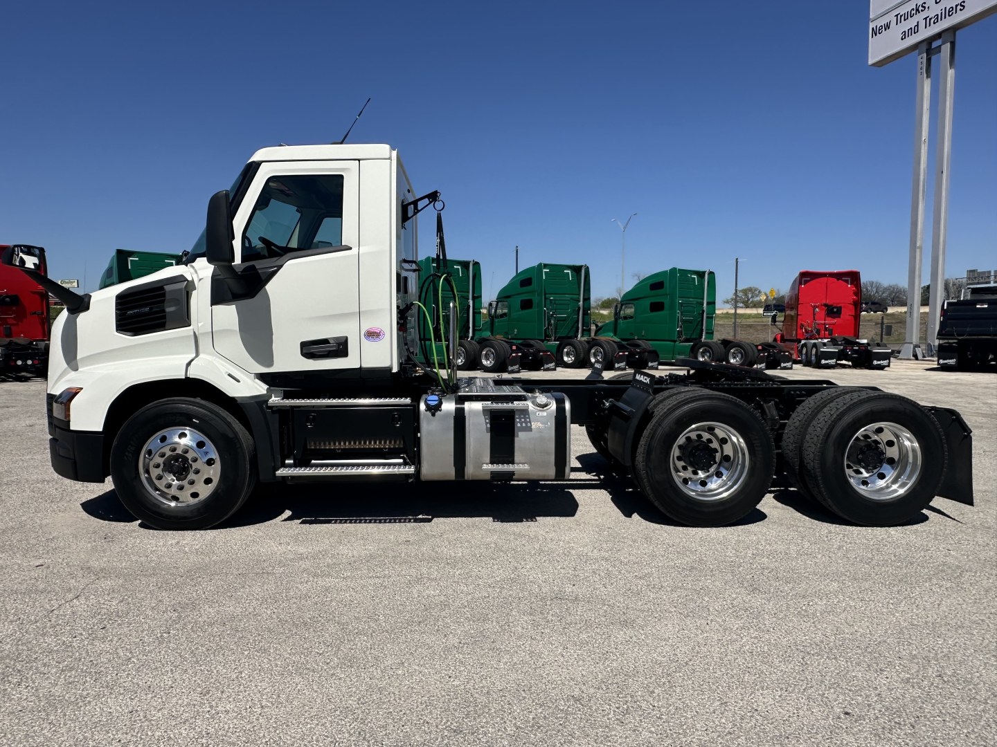 Truck chassis side view showing white Mack AN64T cab with dual rear axles and fuel tanks, highway trailer yard in background.