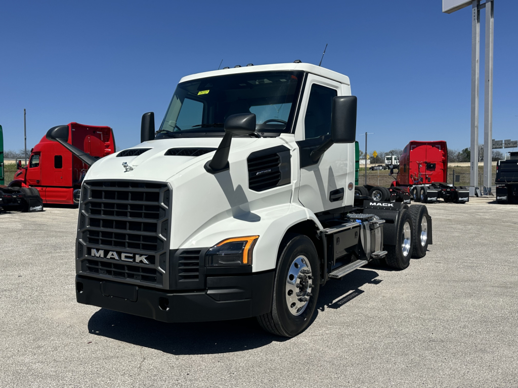 Mack AN64T truck in a lot showing front grille with Mack badge, side profile, white cab, black bumper, dual rear axles, fuel tanks, and mirrors.