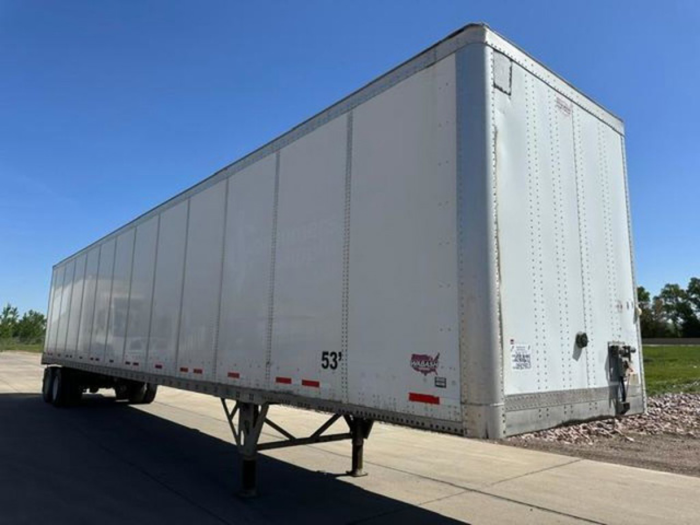 Trailer side and rear into a semi-trailer box showing a white cargo trailer with landing gear and rear doors, 53' length marking visible, no branding.
