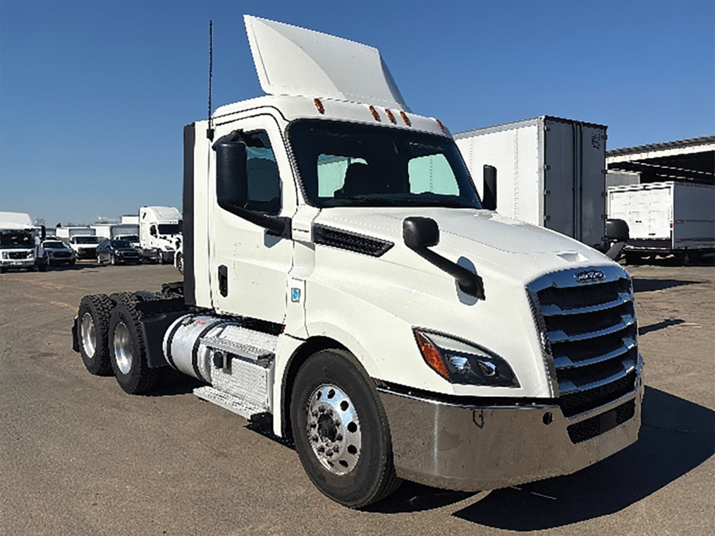 Truck cab in yard showing 2019 Freightliner Cascadia126 with white exterior and raised sleeper, emblem grille, side mirrors, and chassis behind