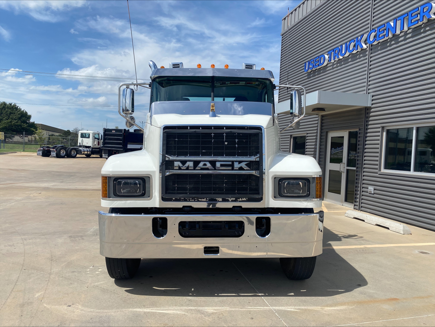 Mack PI64T truck front view in a lot showing grille, headlights, bumper; signage 'USED TRUCK CENTER' on building; chrome front bumper and mirrors visible