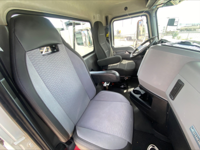 Truck cab interior of a 2021 Mack PI64T showing front bench seat, steering wheel, dashboard, and door panel with light gray upholstery.