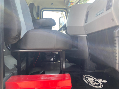 Cab interior of a 2021 Mack PI64T conventional daycab showing driver seat and dashboard area with a red toolbox on the floor near the cab entry.