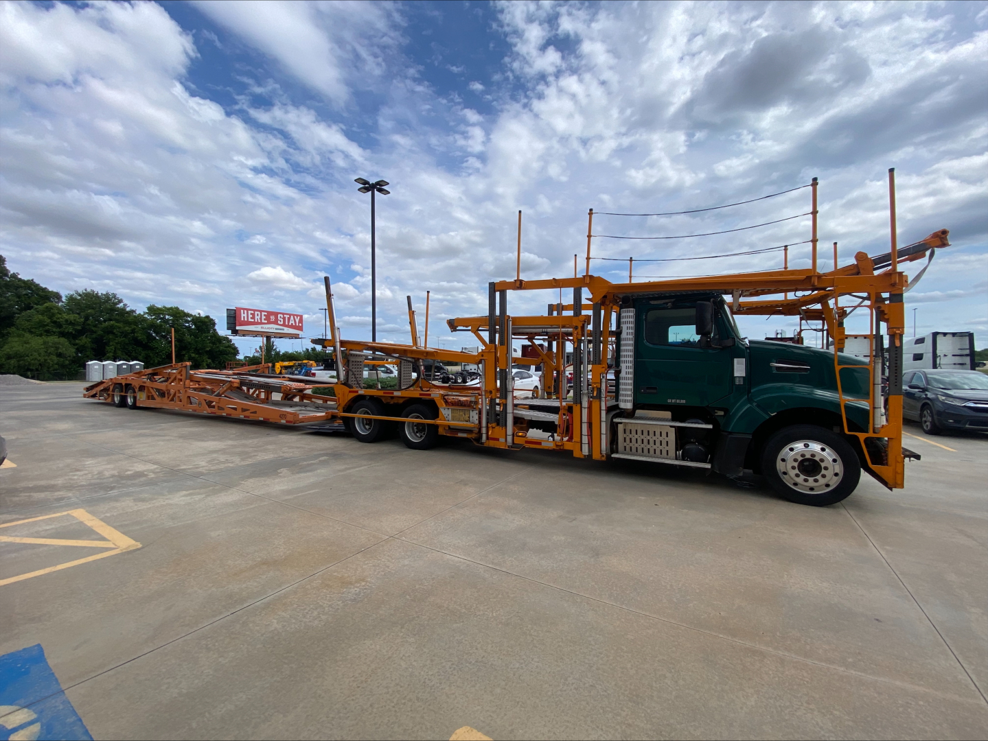 Volvo VAH car carrier truck with an orange car hauling trailer and green cab, side view.