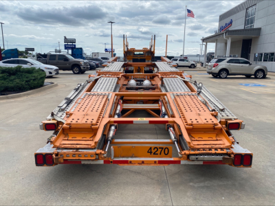 Orange auto carrier trailer back end with metal ramps and numeric 4270 plate, Volvo VAH listing context in dealership lot.