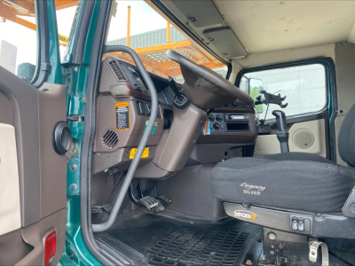 Interior cab of a 2014 Volvo VAH auto carrier showing steering wheel, dashboard, gray seats, and floor mats. Visible text includes ‘Volvo’ on seat cover and control panels.