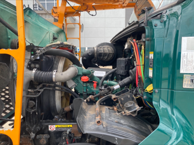 Volvo VAH truck engine bay showing various components: hoses, wiring, air intake, radiator, and green cab with door label visible.