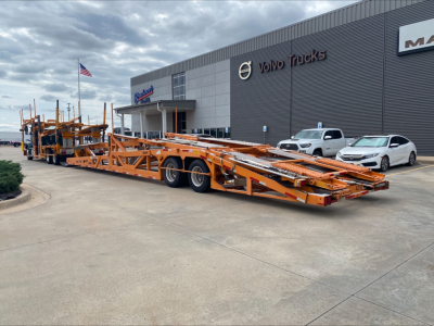 Long orange car hauler trailer attached to a Volvo VAH auto carrier in front of a Volvo Trucks dealership.