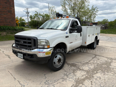 Ford F-450 utility service truck, white, crew cab with service utility bed panels, DOT lights on roof, front grille, bumper, and VIN plate visible.