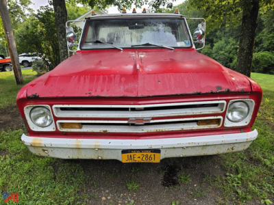 1968 Chevrolet C30 pickup truck front view showing chrome grille, dual round headlights, yellow license plate, and red body with some corrosion near bumper.