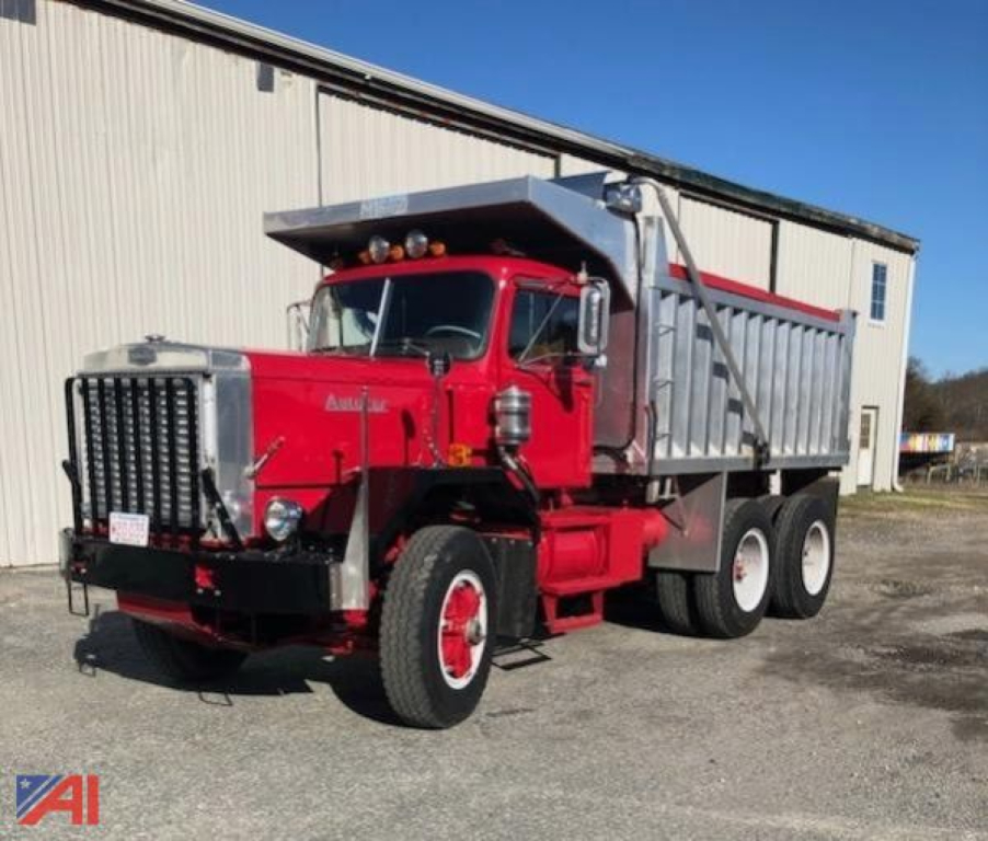 Dump truck in red with silver dump bed showing Autocar DC9964 branding and front grille