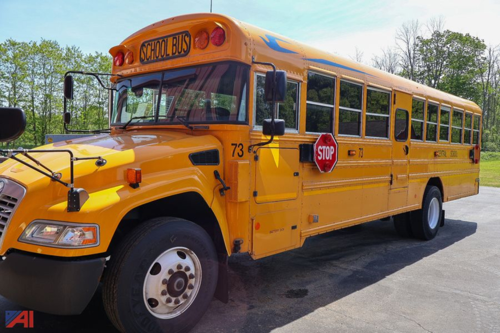 School bus showing front-left view with yellow body, black bumper, and stop sign; 'SCHOOL BUS' sign on top; blue Bird logo not visible