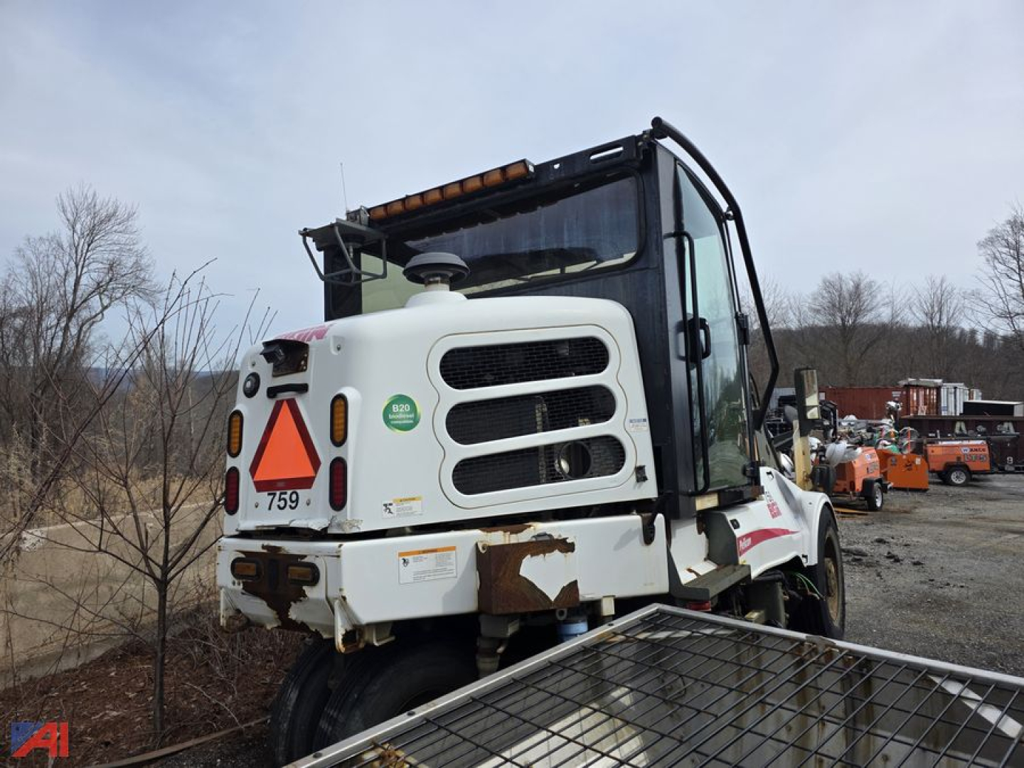 Elgin sweeper truck cab front view showing white body with black grille, orange warning triangle at rear, and damaged lower panel.