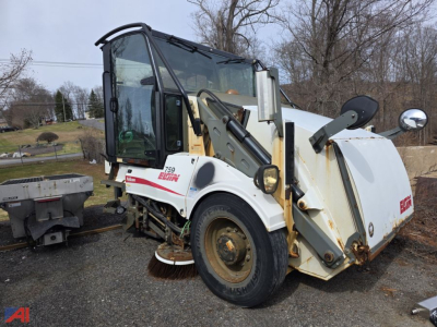 Elgin sweeper truck side view showing side-mounted sweeping arm and brush housing, front cab with windows, white body with red Elgin logo, rusted wheels.