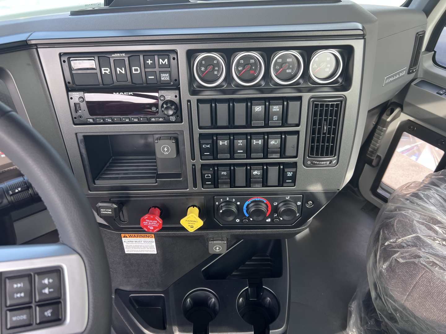 Mack PI64T dash area showing gauges and controls with gear selector, climate controls, and multiple switches.