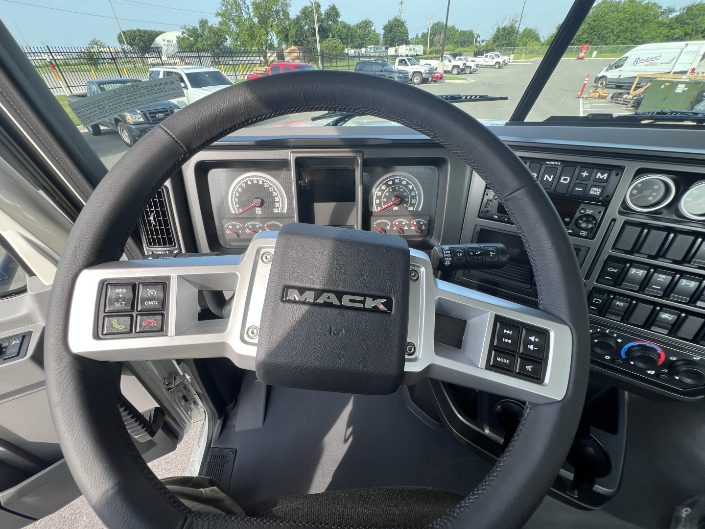 Mack PI64T truck interior showing steering wheel with Mack logo, dashboard gauges, and control stalks.