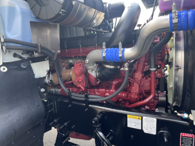 Mack PI64T engine bay with red engine block, silver intake, blue hoses, and black surrounding components.