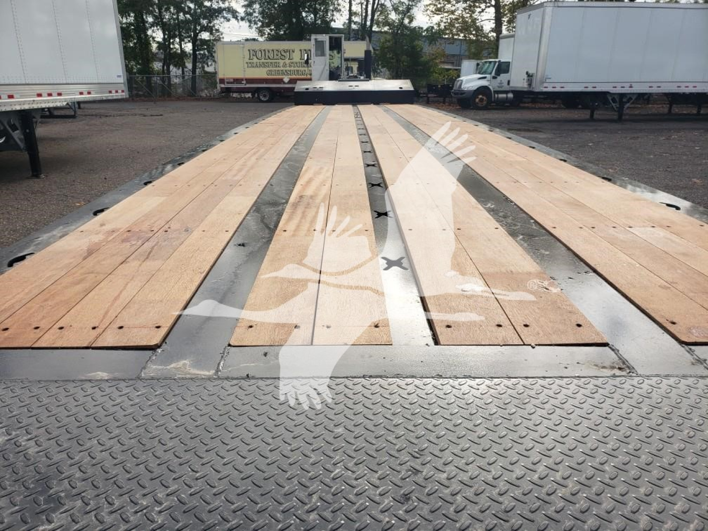 Trailer deck with wooden planks and metal support beams, viewed from the front, showing long flatbed surface and diamond plate near the edge.