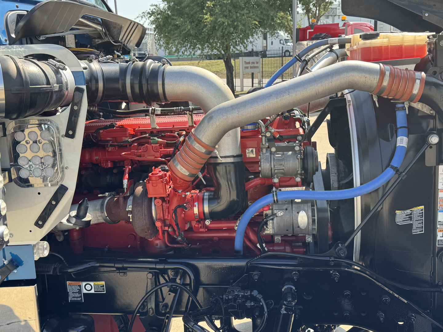 Kenworth W900L engine bay showing red engine, large silver exhaust manifolds, and blue hoses with black chassis.