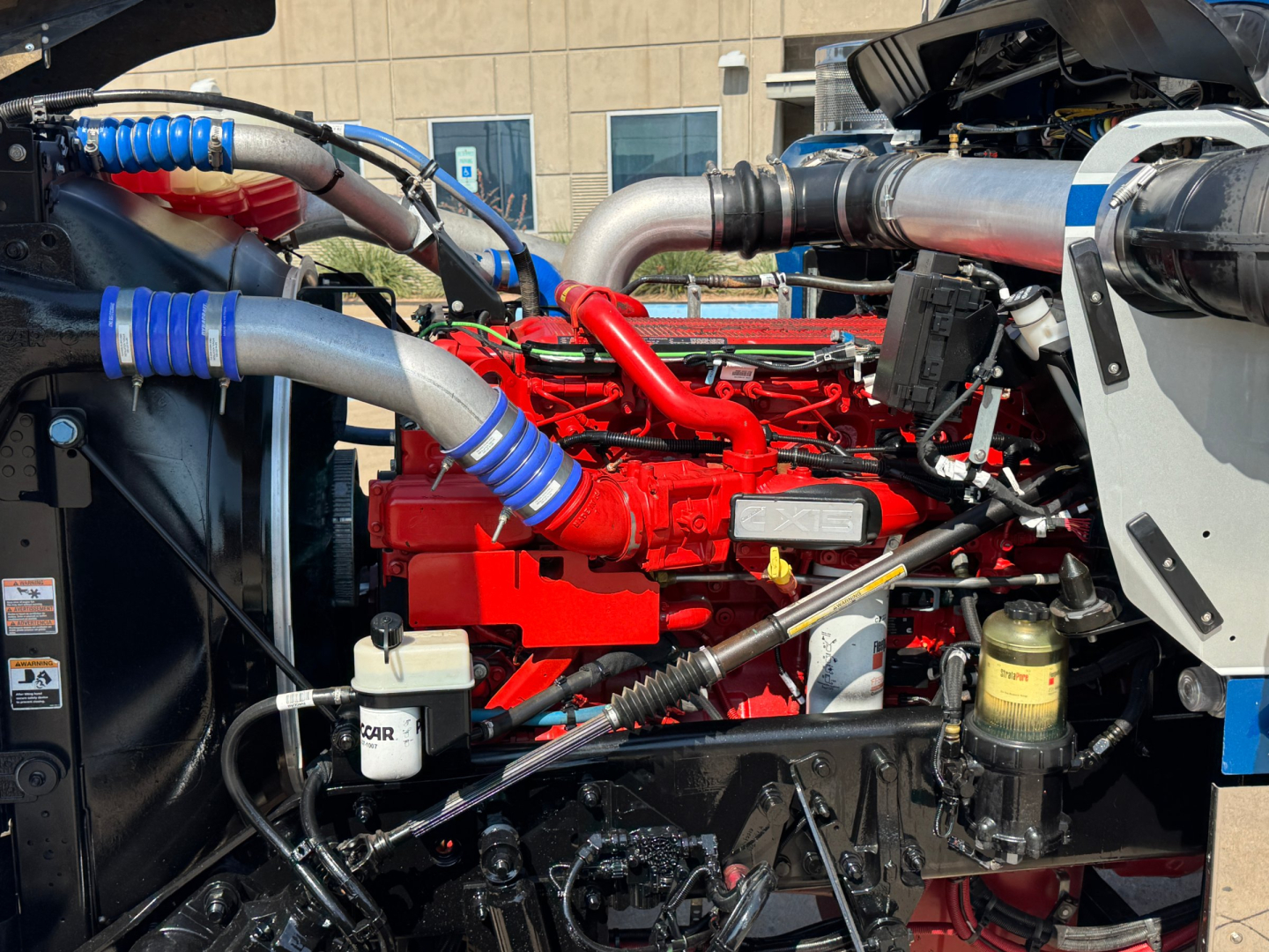 Kenworth W900L engine bay with red engine, blue silicone hoses, silver intercooler piping, and black chassis components visible.