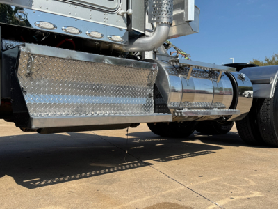 Kenworth W900L truck side view showing polished chrome fuel tanks and diamond plate side panels.