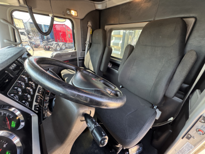 Kenworth W900L truck interior showing steering wheel, driver seat and dashboard with gauges; window and door panel visible.
