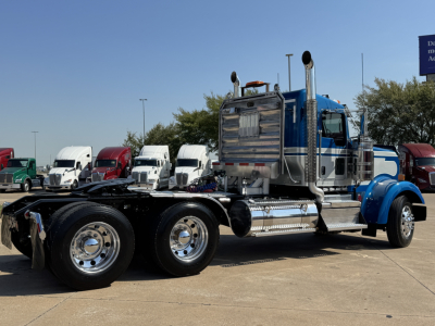 Kenworth W900L conventional daycab tractor in blue and chrome, side view showing dual rear axles, exhaust stacks, fuel tanks, and chrome details.
