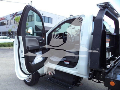 Truck cab interior with open door showing steering wheel and dashboard, white exterior, rollback equipment mounted at rear.