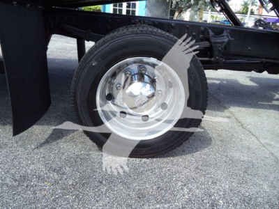 Wheel and part of truck chassis with steel rim and black tire visible under a truck frame.