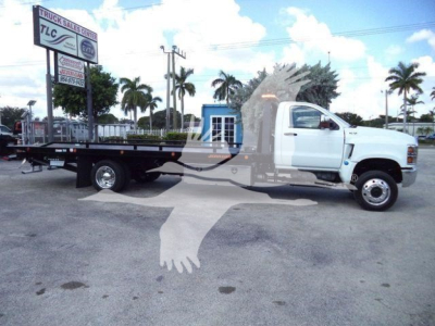 Flatbed tow truck with white cab and black flatbed, dealership sign in background. VIN visible text overlay on image.