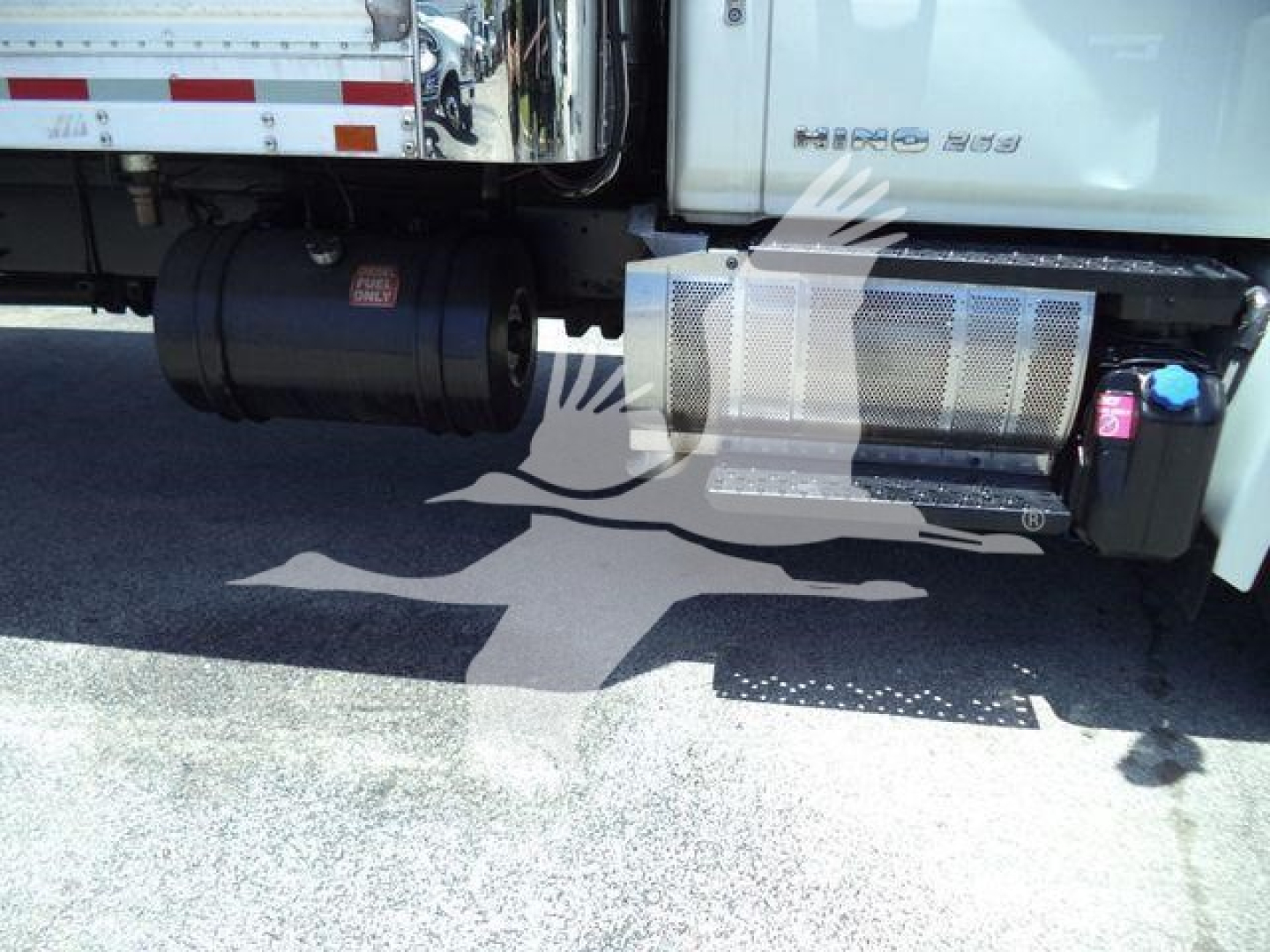 Truck side view showing large cylindrical exhaust and a metal mesh step cover under the cab of a 2019 Hino 268A refrigerated truck.